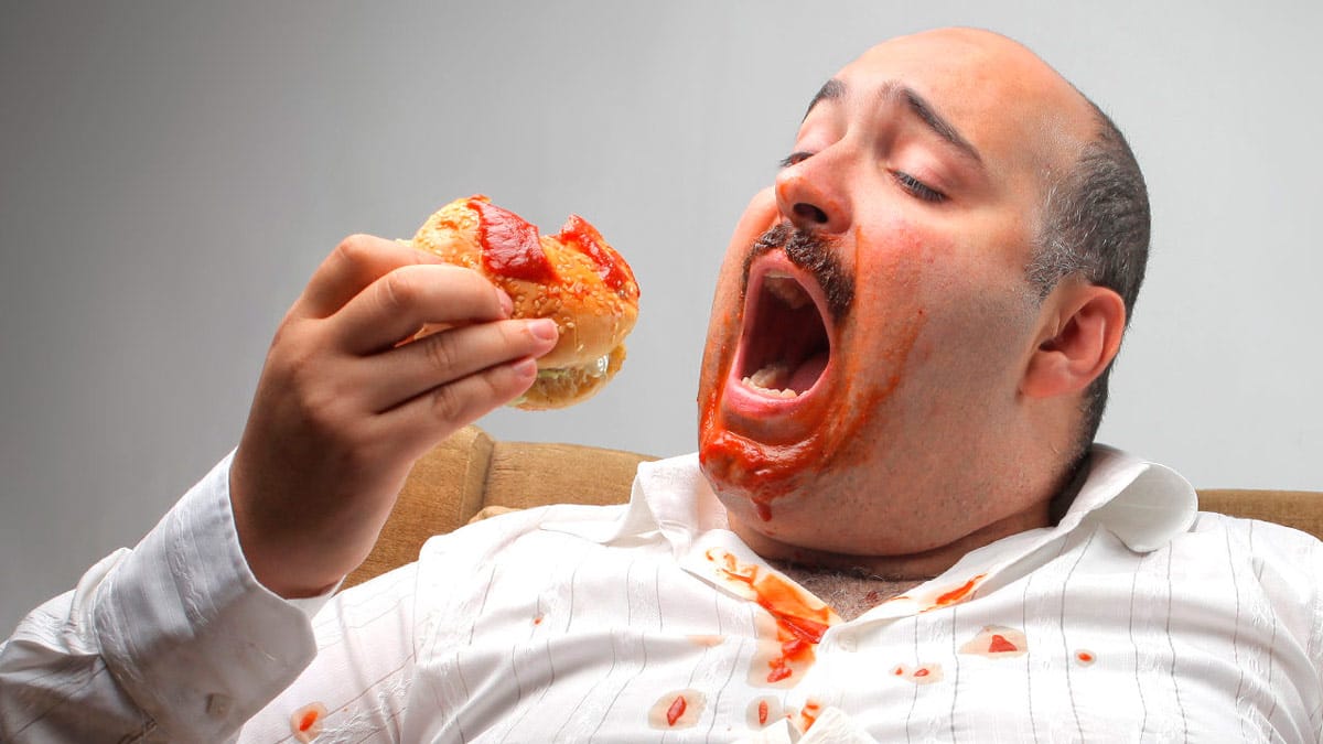 Compulsão Alimentar Periódica: Tudo Sobre a Doença! Homem comendo hambúrguer e sujo de ketchup
