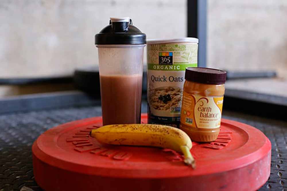 Alimentação Pós-Treino RECOMENDADA Segundo Pesquisas! Anilha com coqueteleira, aveia e pasta de amendoim, representando o ideal da alimentação pós-treino