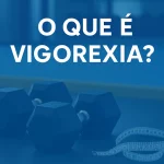 Dois halteres pretos sobre o chão da academia ao lado de uma fita métrica enrolada, com espelho ao fundo e a frase 'O que é vigorexia?' em destaque sobre fundo azul